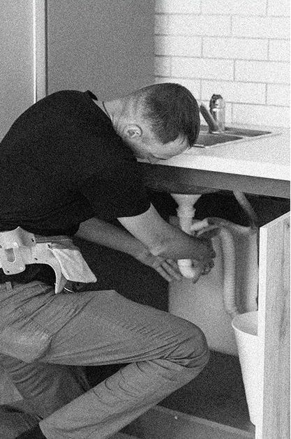 A man is fixing a sink in a black and white photo.