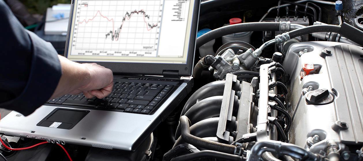 A man is working on a car engine with a laptop