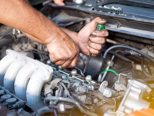 A man is working on a car engine with a screwdriver.
