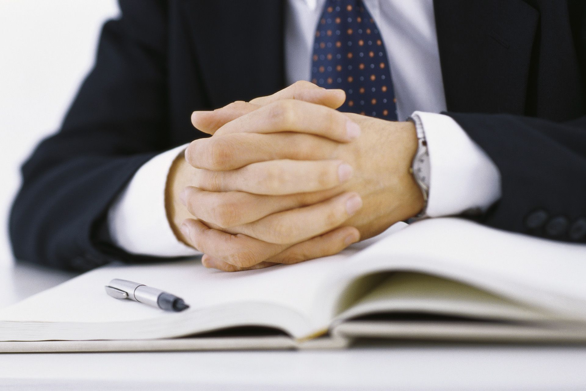 A man in a suit and tie is sitting at a desk with his hands folded