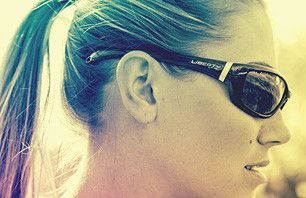 A woman wearing sunglasses and a ponytail is smiling.