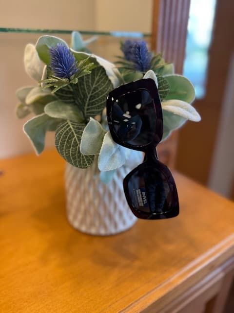 A pair of sunglasses is sitting on a table next to a vase of flowers.