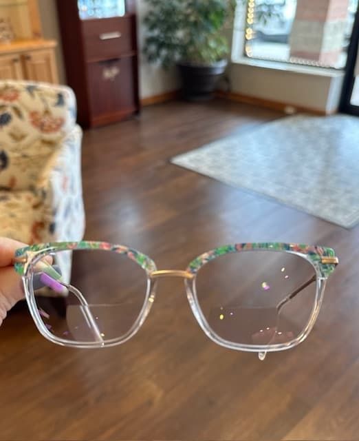 A person is holding a pair of glasses in a living room.