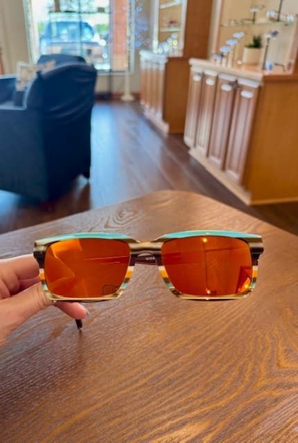 A person is holding a pair of sunglasses on a wooden table.