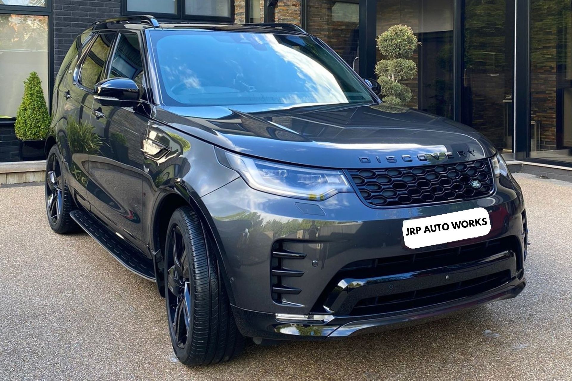 Dark gray SUV parked outside a building, front view with dealership plate.