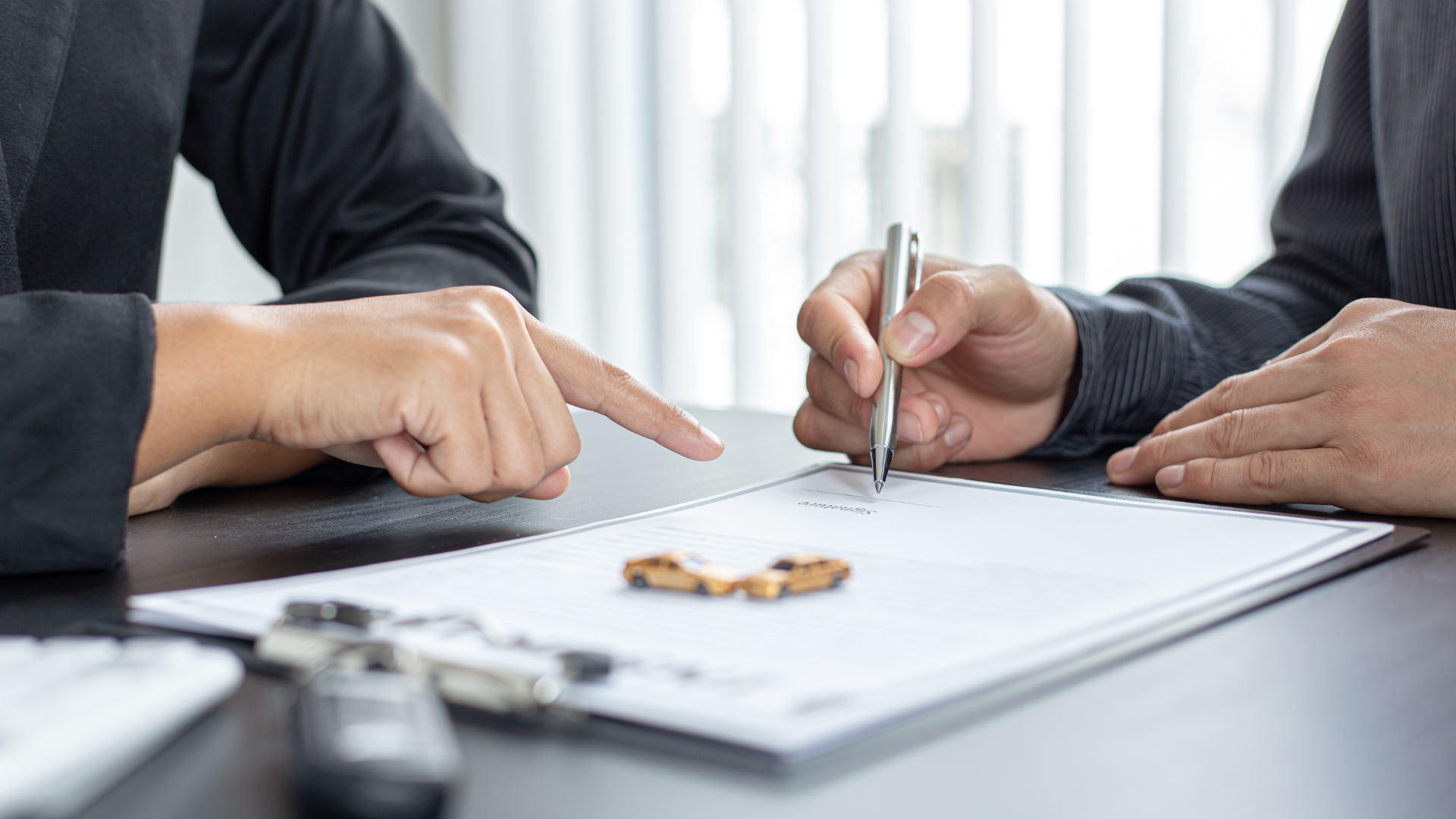 Hands pointing at document, person signing with pen. Car keys on the paper.