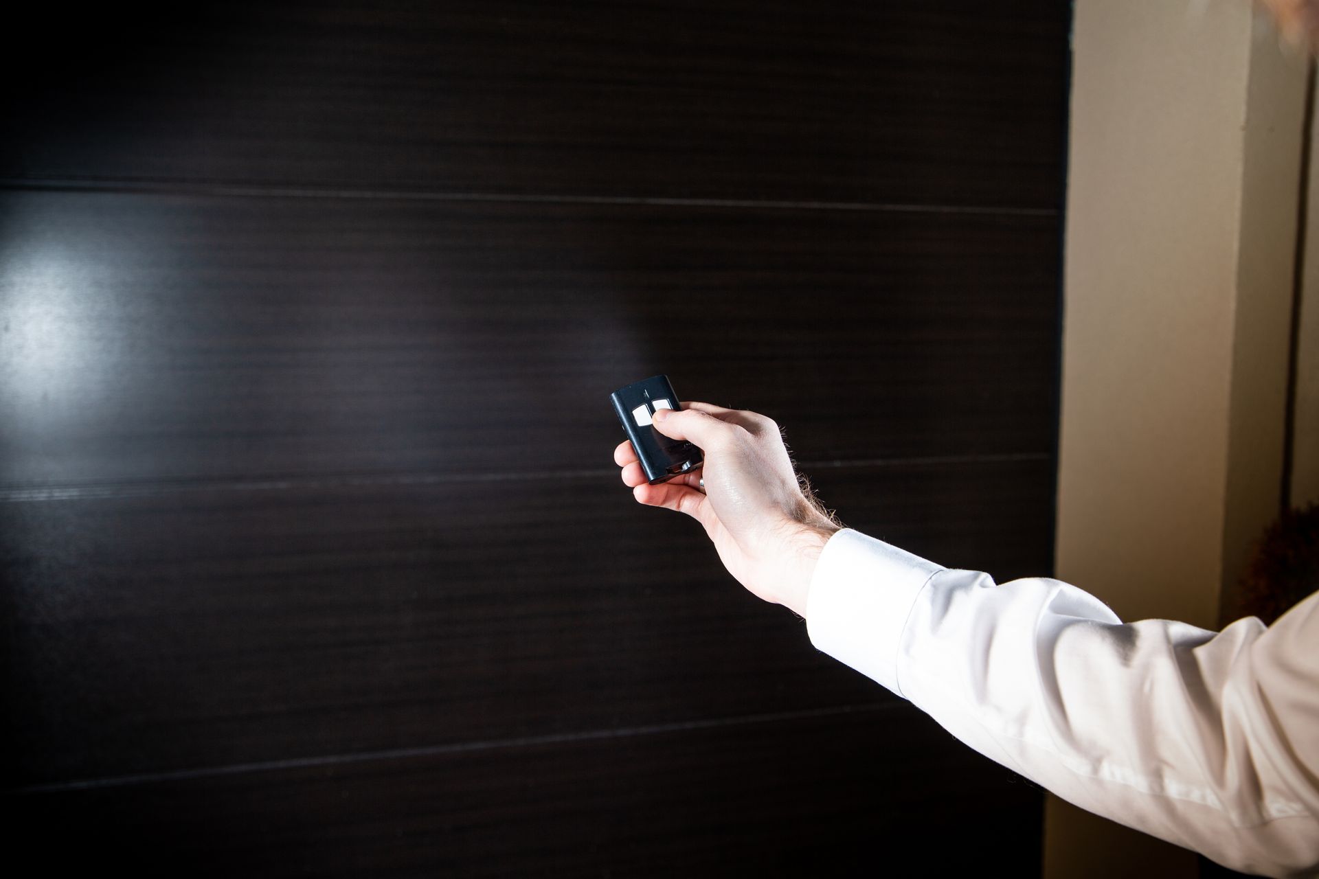 Hand holding a remote control aimed at a dark automatic garage door or shutter.