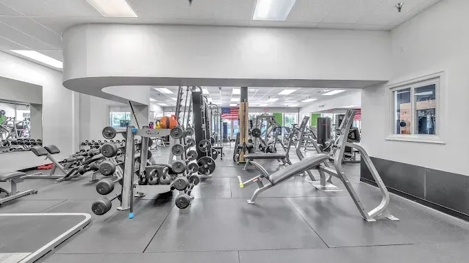 Gym interior with weight racks, exercise machines, and mirrors.