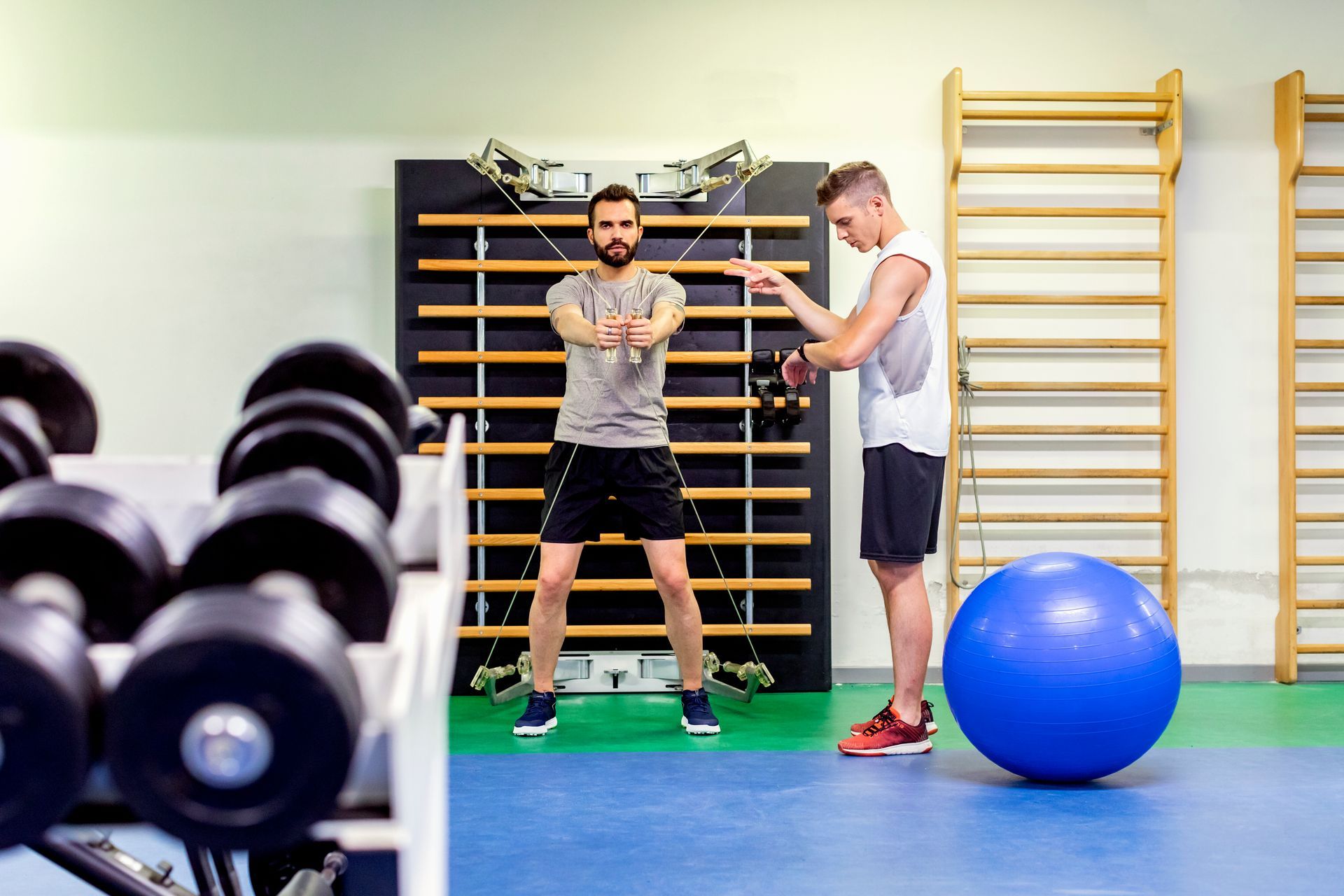 A man is doing exercises with a personal trainer in a gym.