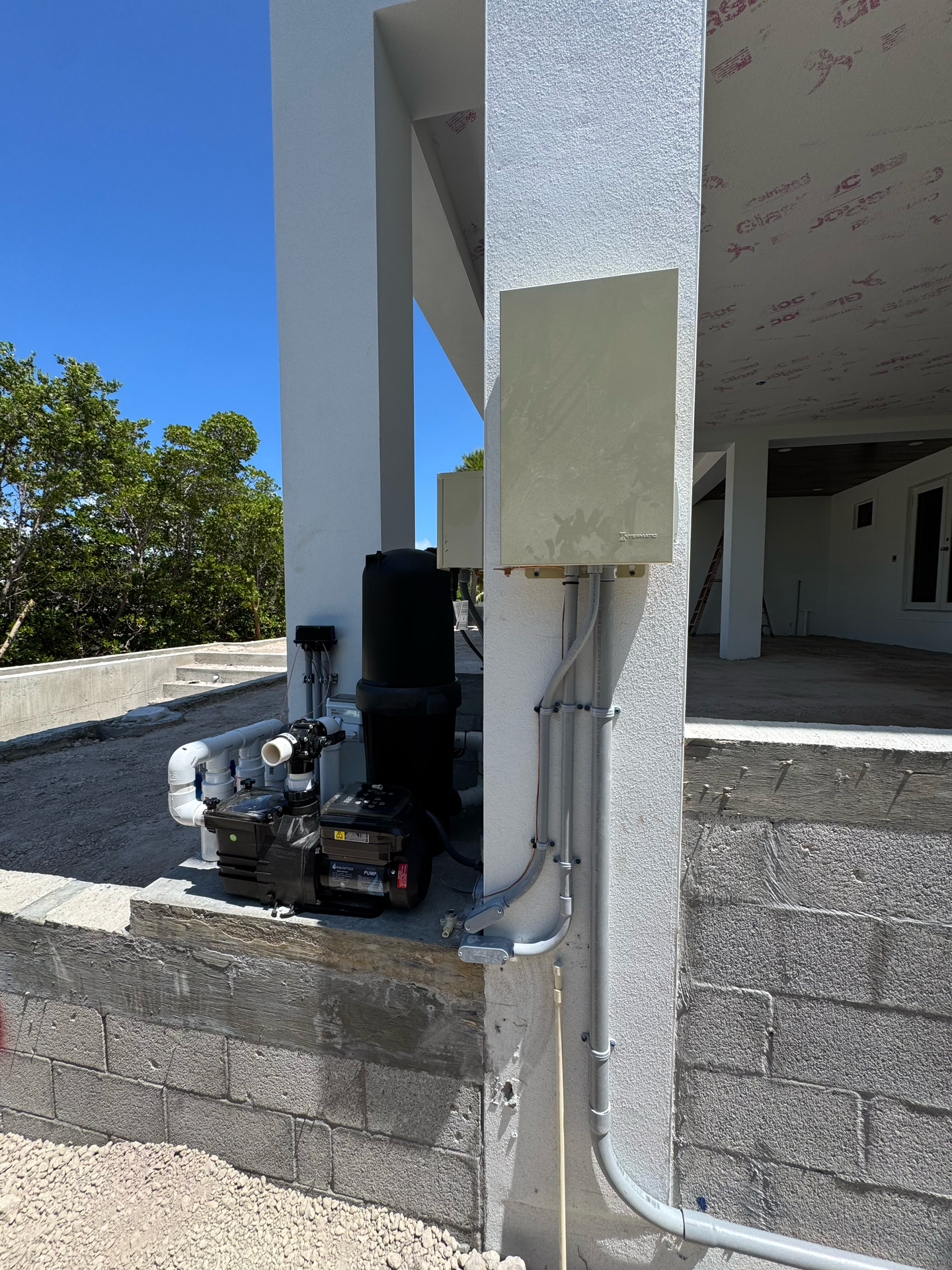 Outdoor electrical panel and conduit on a white pillar next to a pump and filter system.