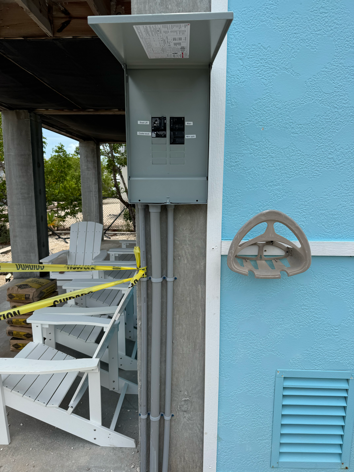 Gray electrical panel mounted on a light blue building, next to conduit and a decorative wheel.