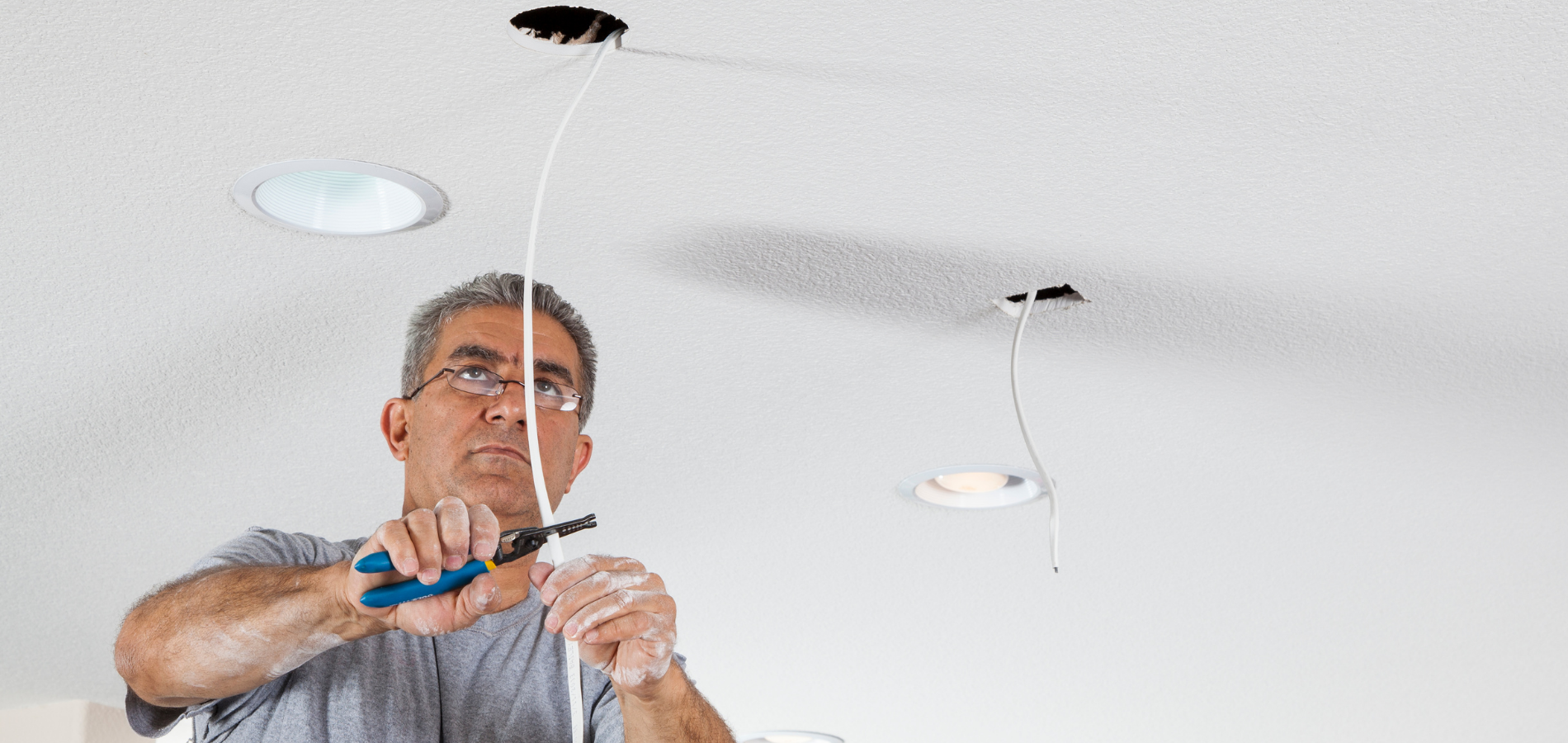 Man cutting wires on a ceiling for electrical work.