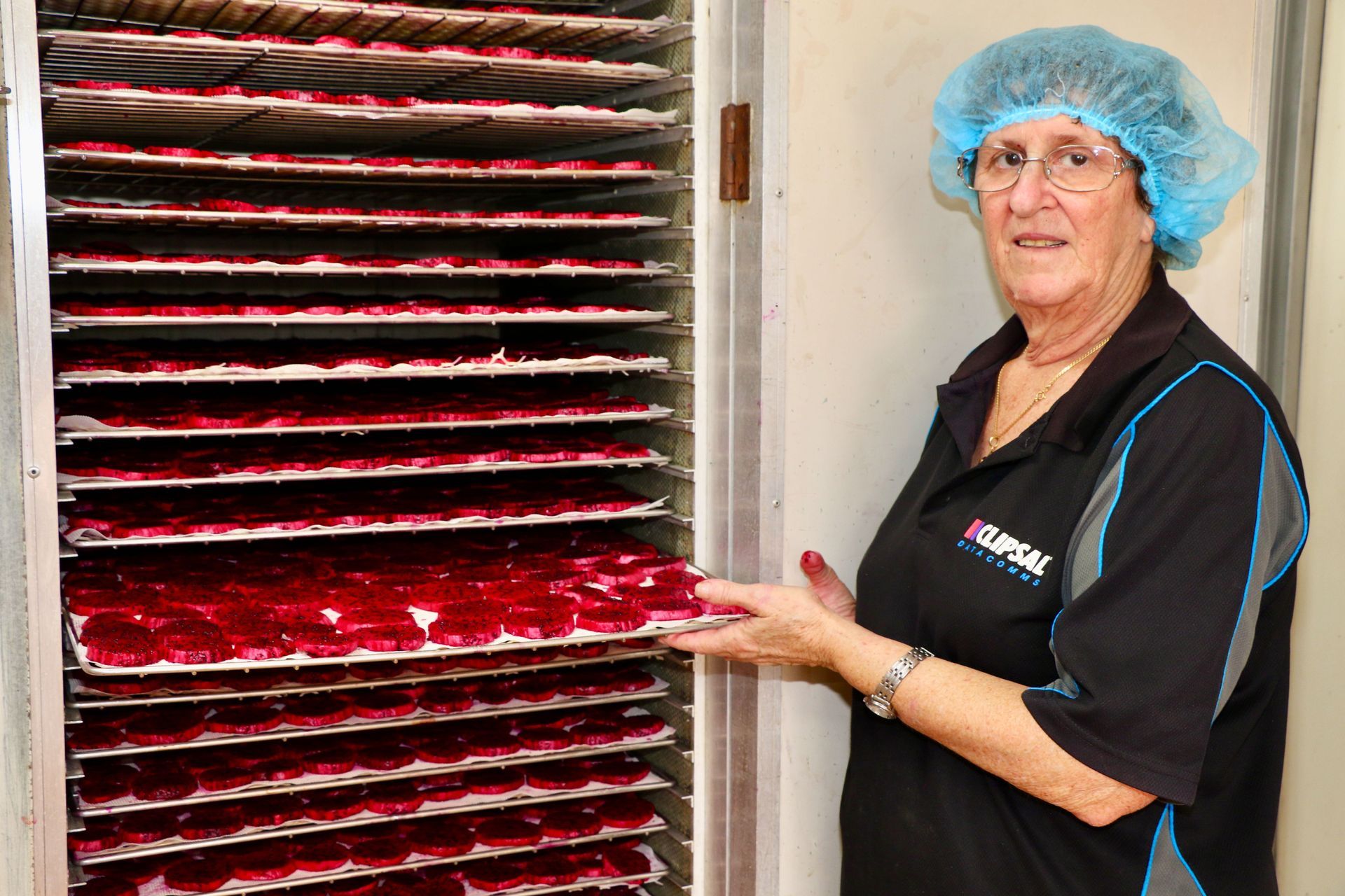 A Woman Wearing a Blue Hat is Standing in Front of a Rack of Food — Mareeba Golden Dried Mangoes in Mareeba, QLD