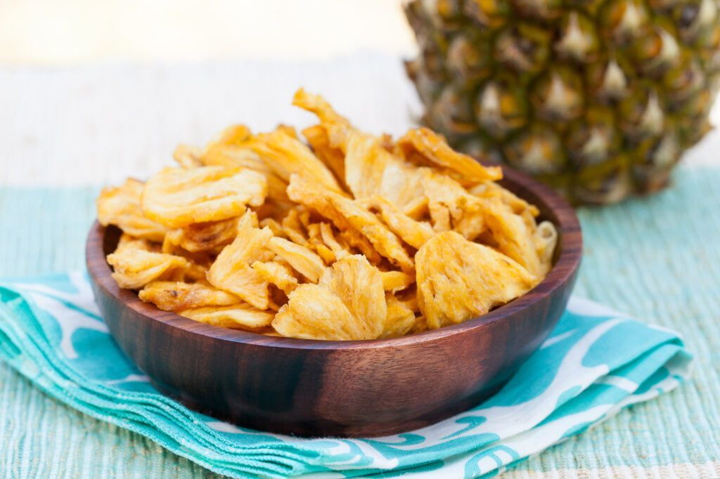 A Bowl of Pineapple Chips is Sitting on a Table Next to a Pineapple — Mareeba Golden Dried Mangoes in Cairns, QLD