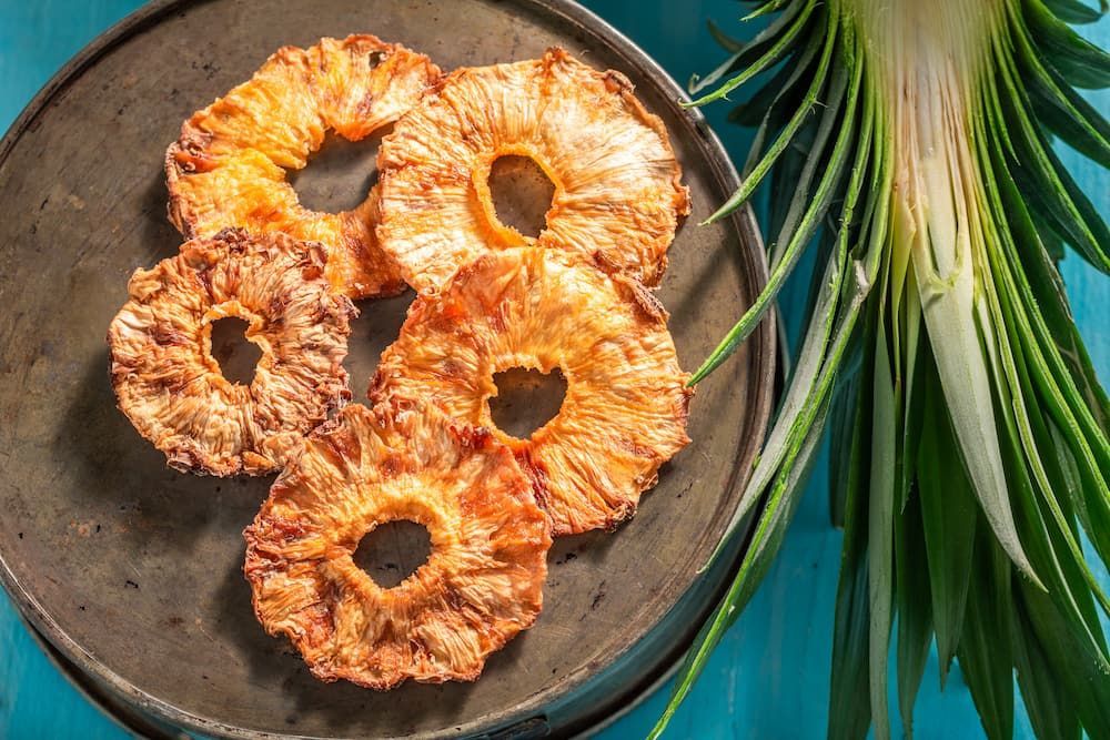 A Plate of Pineapple Rings on a Table Next to a Pineapple Plant — Mareeba Golden Dried Mangoes in Gold Coast, QLD