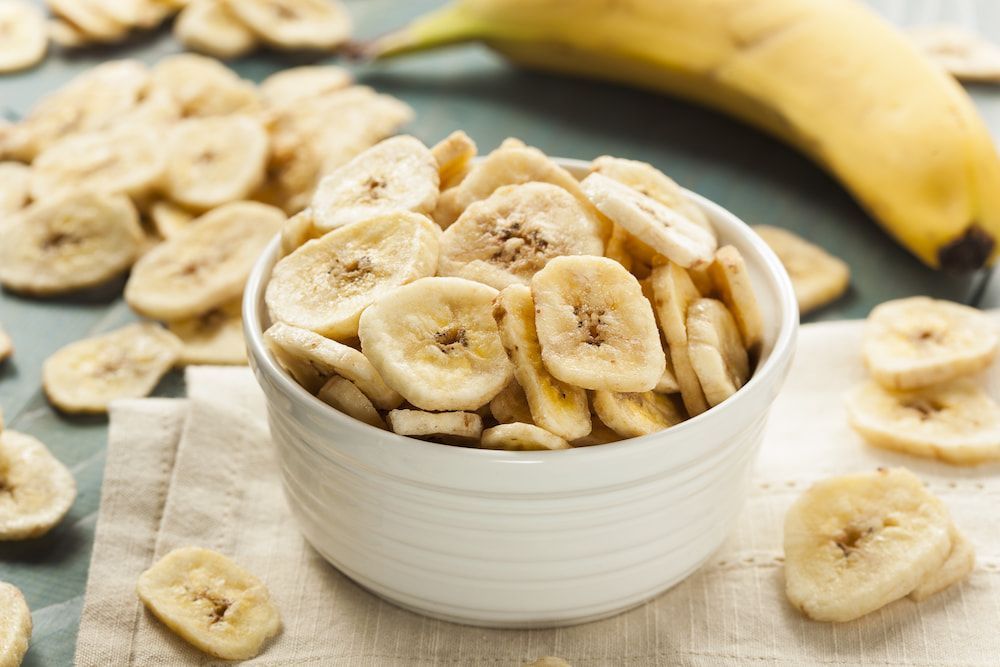There is a Bowl of Banana Chips Next to a Banana — Mareeba Golden Dried Mangoes in Cairns, QLD