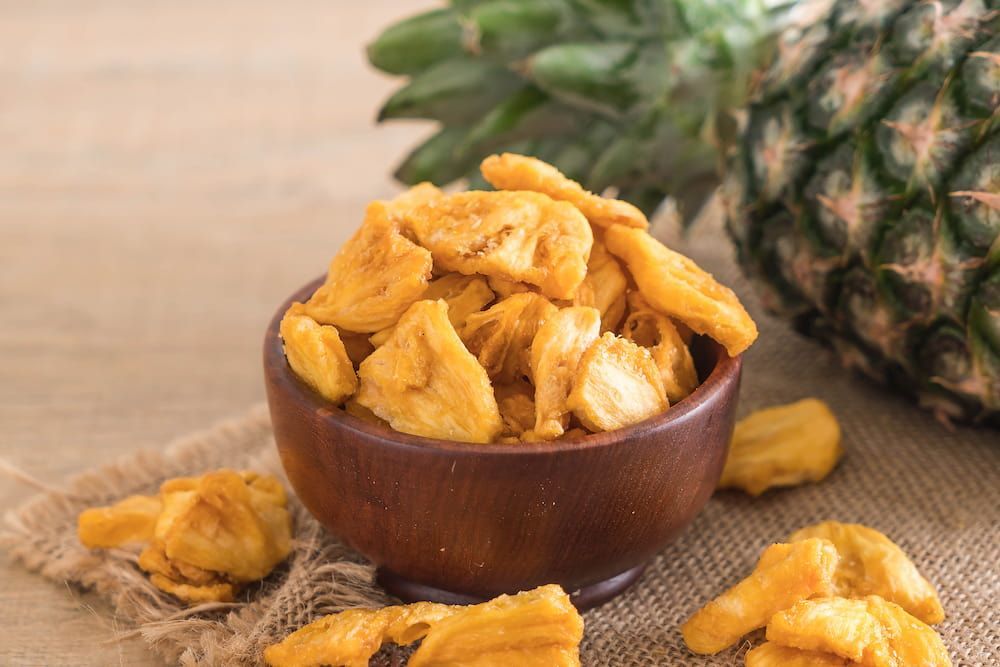 A Wooden Bowl Filled With Dried Pineapple Chips Next to a Pineapple — Mareeba Golden Dried Mangoes in Sunshine Coast, QLD