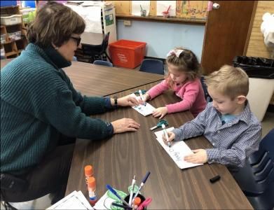 A woman and two children are sitting at a table drawing with markers.