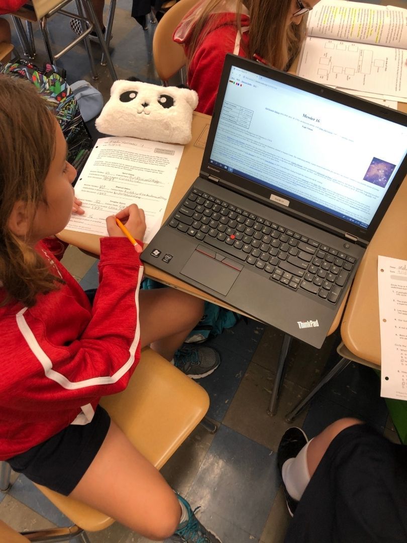 A girl in a red jacket sits at a desk with a laptop