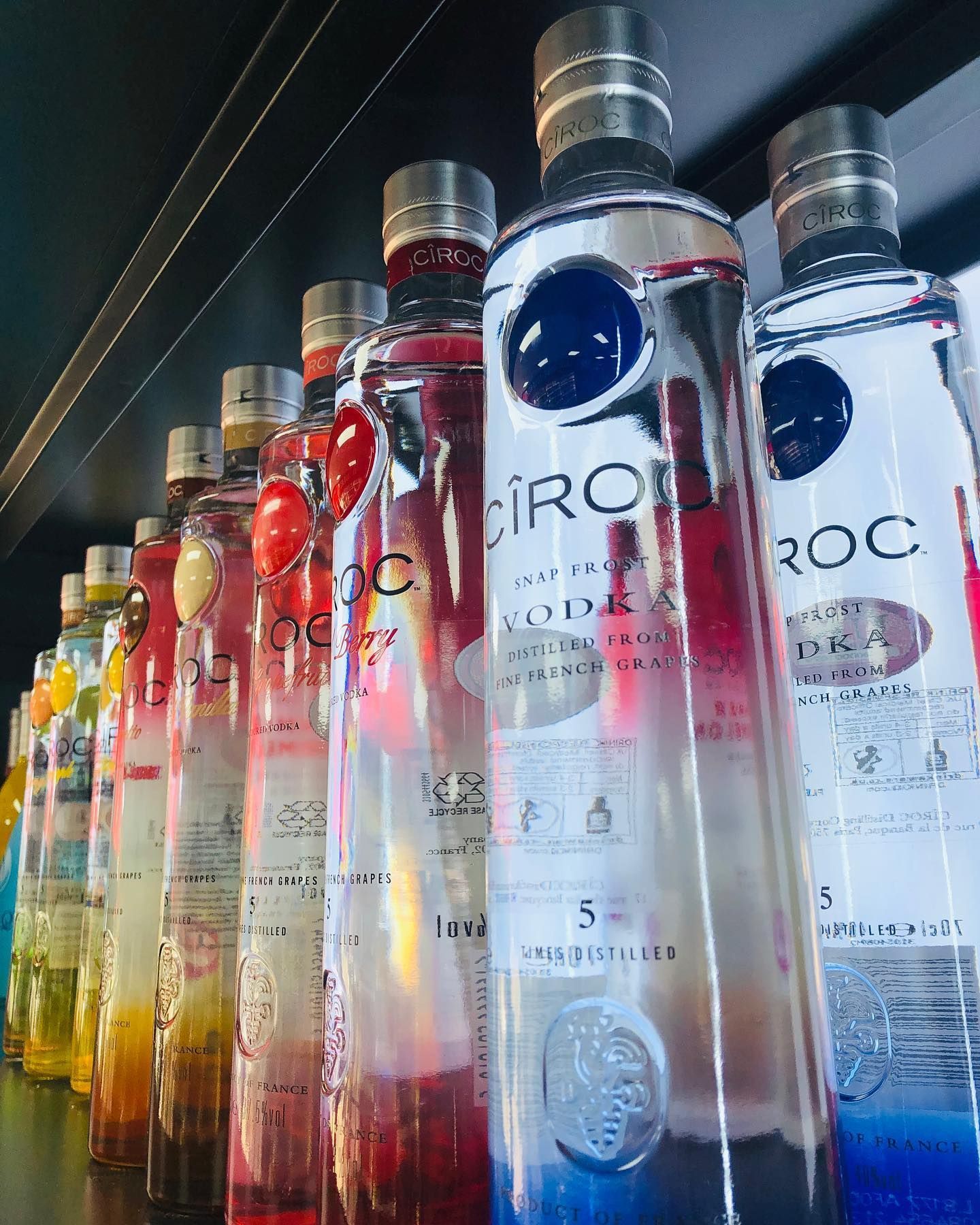 A row of bottles of ciroc vodka are lined up on a shelf.