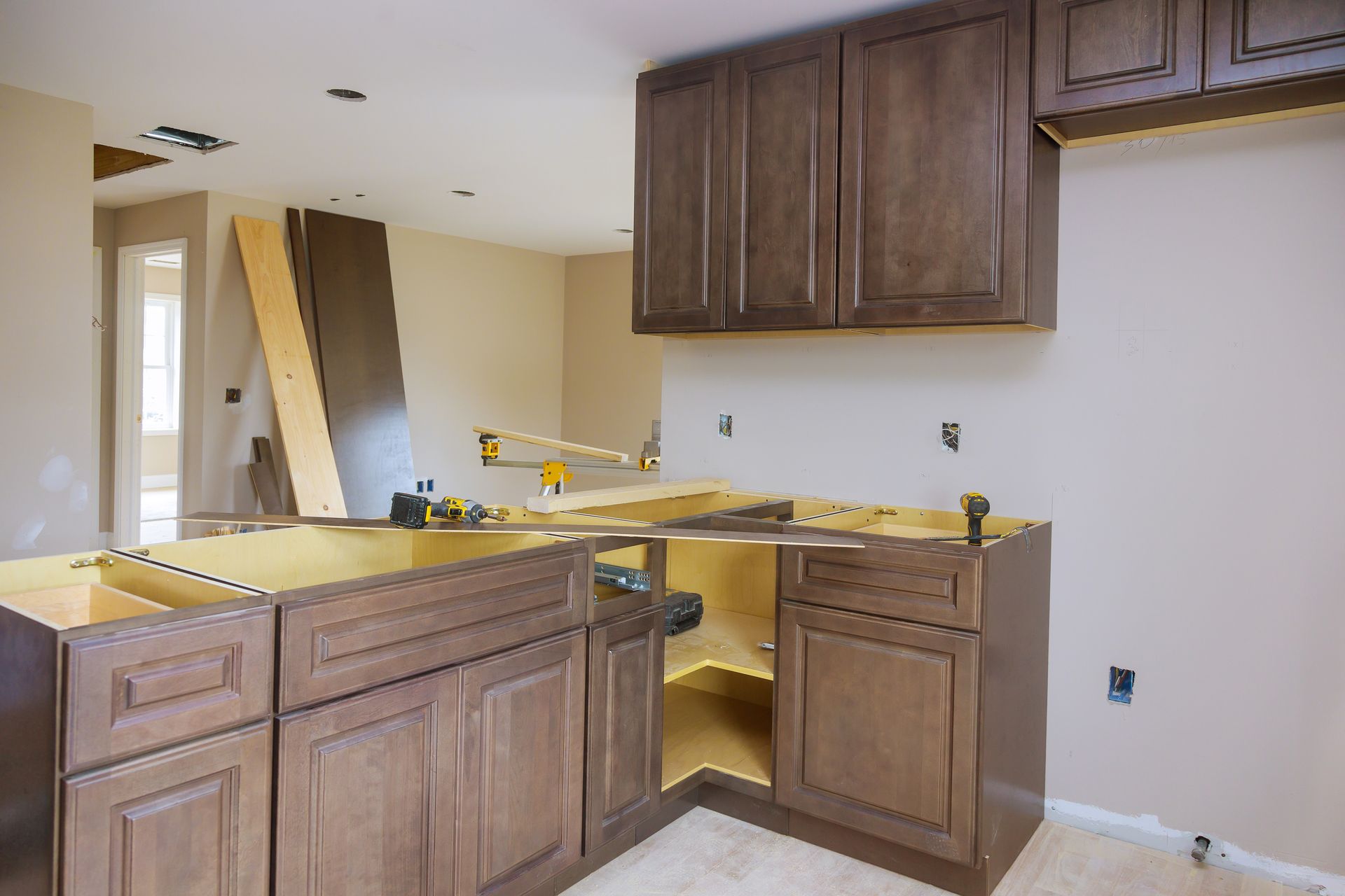 Kitchen cabinets being installed in a room. Brown cabinets, tan walls, tools visible.