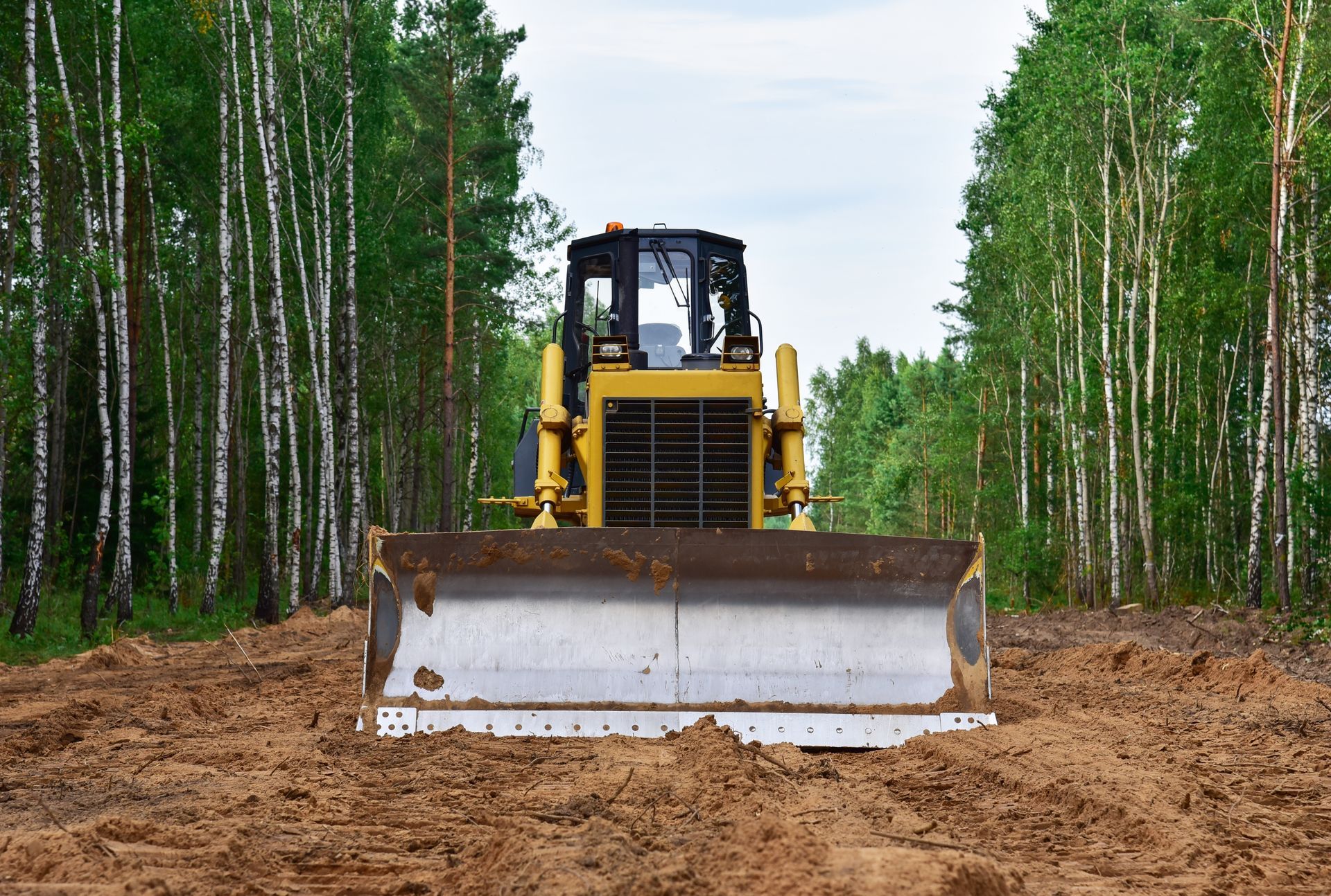 Yellow bulldozer clearing dirt path through a forest.