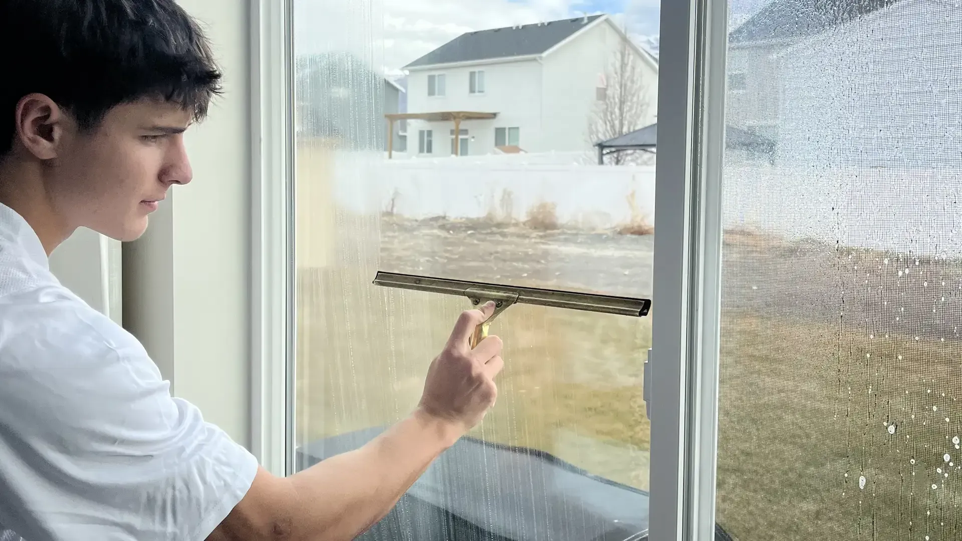 A young man is cleaning a window with a squeegee.