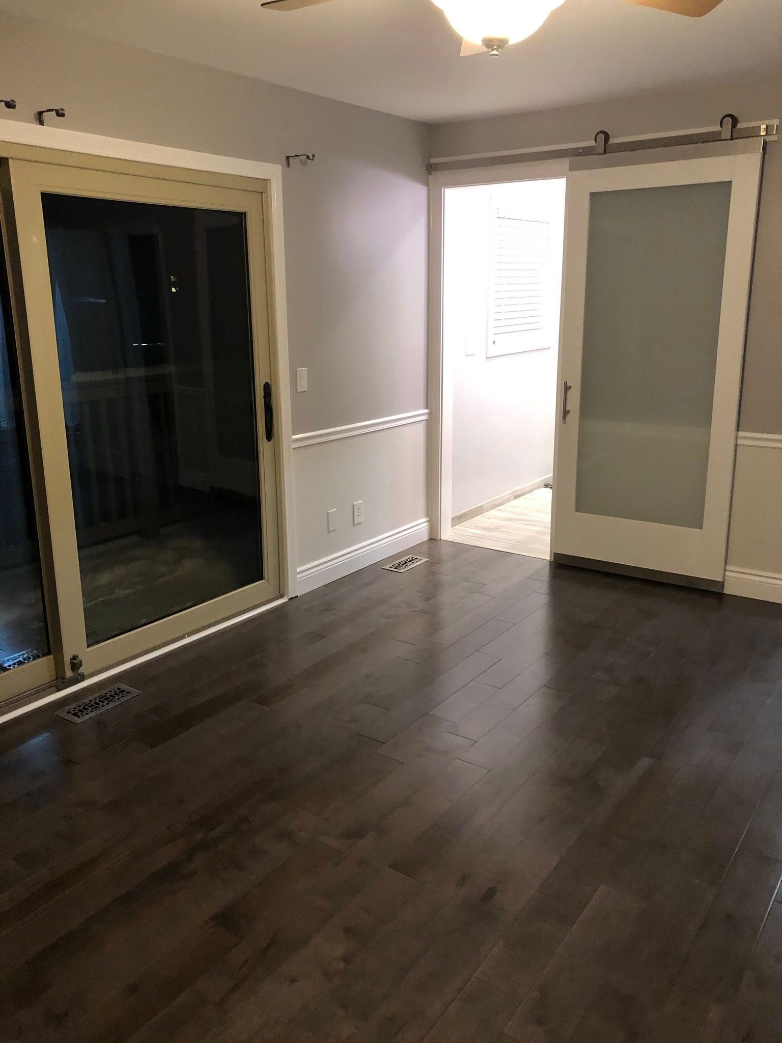 Empty room with dark wood floors, sliding glass door, and a frosted glass sliding barn door.