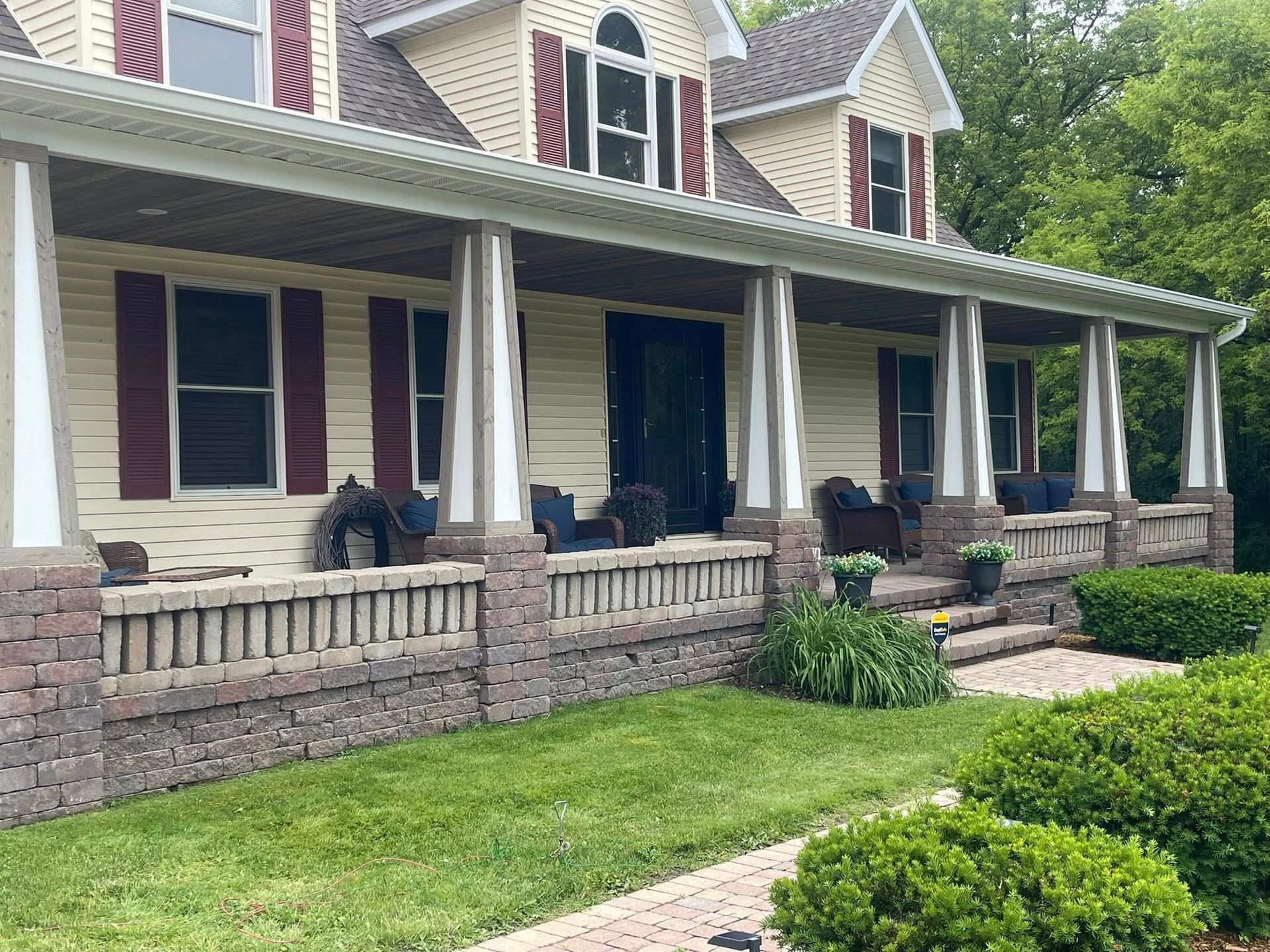 House with a large porch, brick and siding exterior, green lawn, red shutters, and steps.