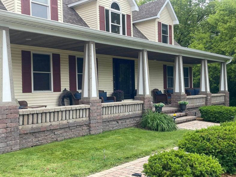 House with a large porch, brick and siding exterior, green lawn, red shutters, and steps.