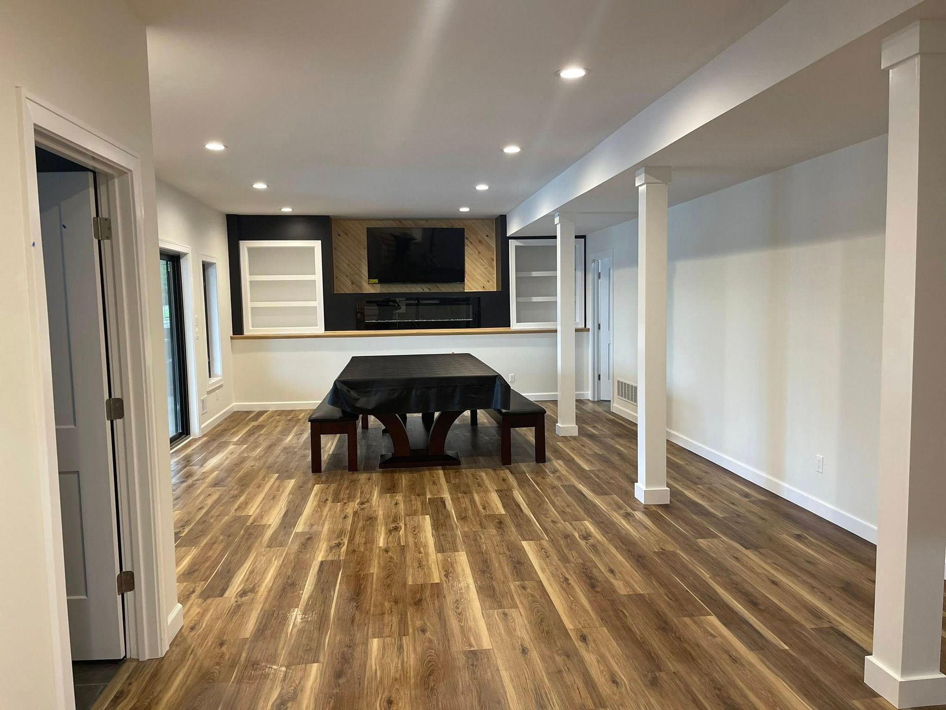 Spacious, finished basement with wood floors, fireplace, and dining area. White walls and columns, natural light.