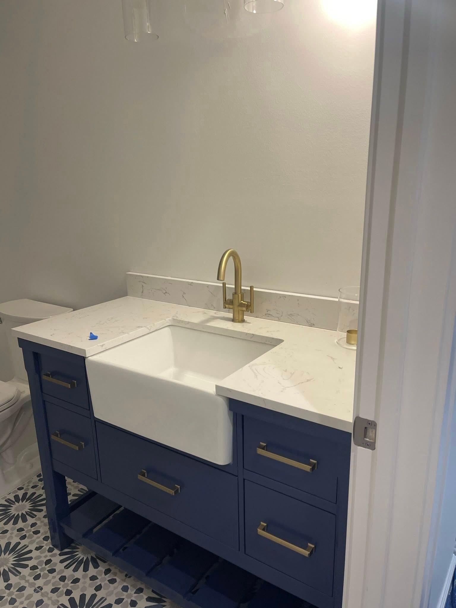 Navy blue bathroom vanity with white countertop, gold faucet, and farmhouse sink.