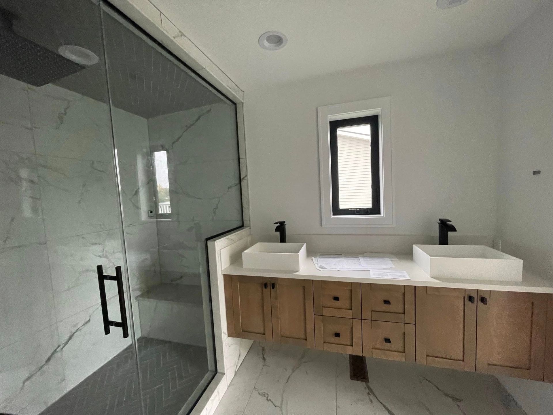 Modern bathroom with glass shower, floating vanity with two sinks, and a window.