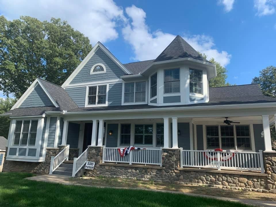 Blue house with white trim, stone base, porch with white railing and bunting, turret.