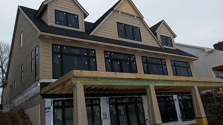 Two-story house under construction with tan siding, black windows, and a partially built deck.