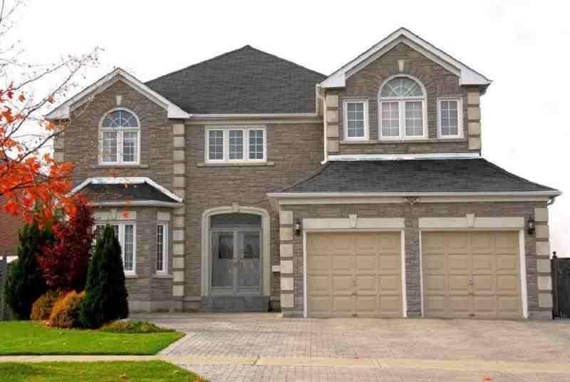 Two-story brick house with a two-car garage, beige doors, and a paved driveway; fall foliage in the front yard.