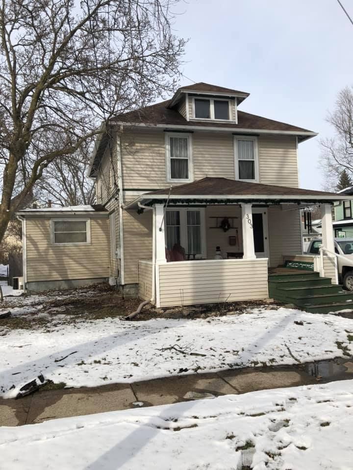 Two-story house with tan siding, porch, and snow-covered ground.