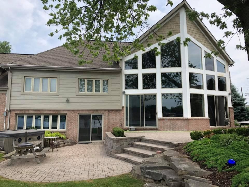 Back exterior of a house with large windows, brick patio, steps, and a hot tub.
