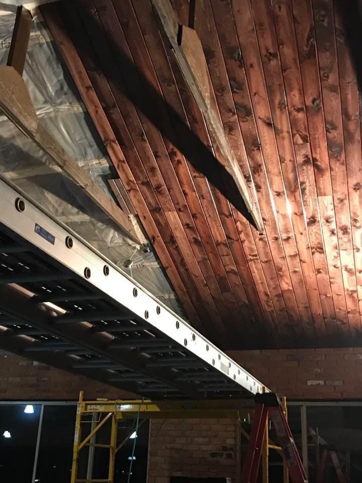 A person on a ladder working on a wooden ceiling with a metal scaffold underneath.