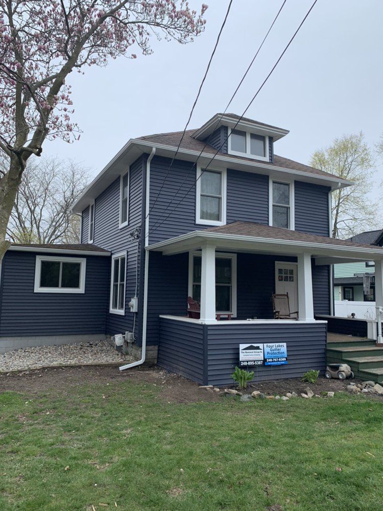Two-story blue house with white trim and a porch under an overcast sky.