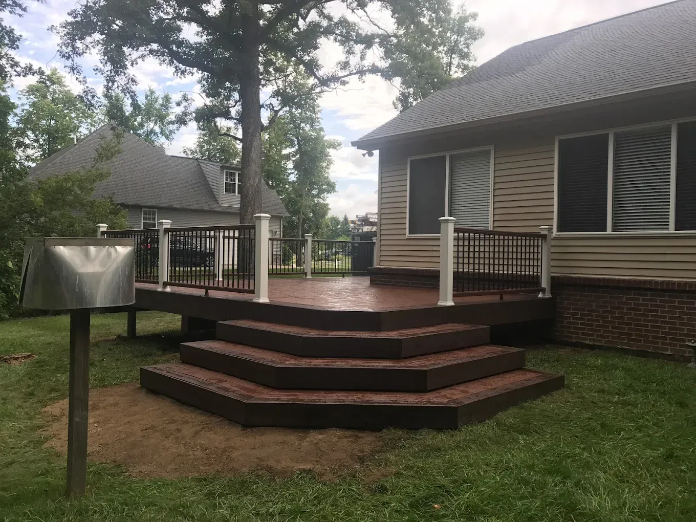 Wooden deck with stairs leading down to a grassy lawn next to a house with windows.