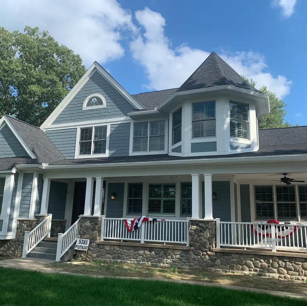 Blue house with white trim, porch, and a turret, against a blue sky.