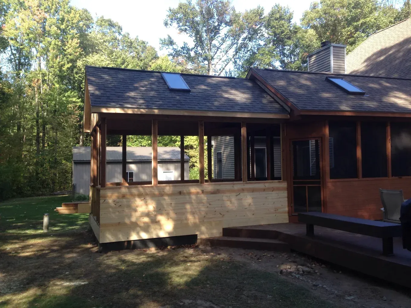 Screened porch addition with wooden frame and light tan siding, attached to a house with skylights.