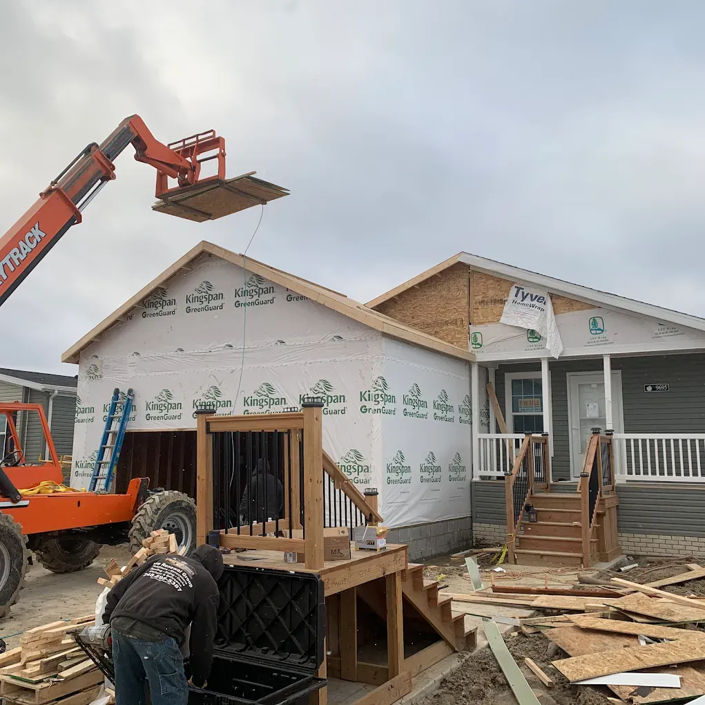 Construction site: A worker using a telehandler to install a roof. House under construction, cloudy sky.