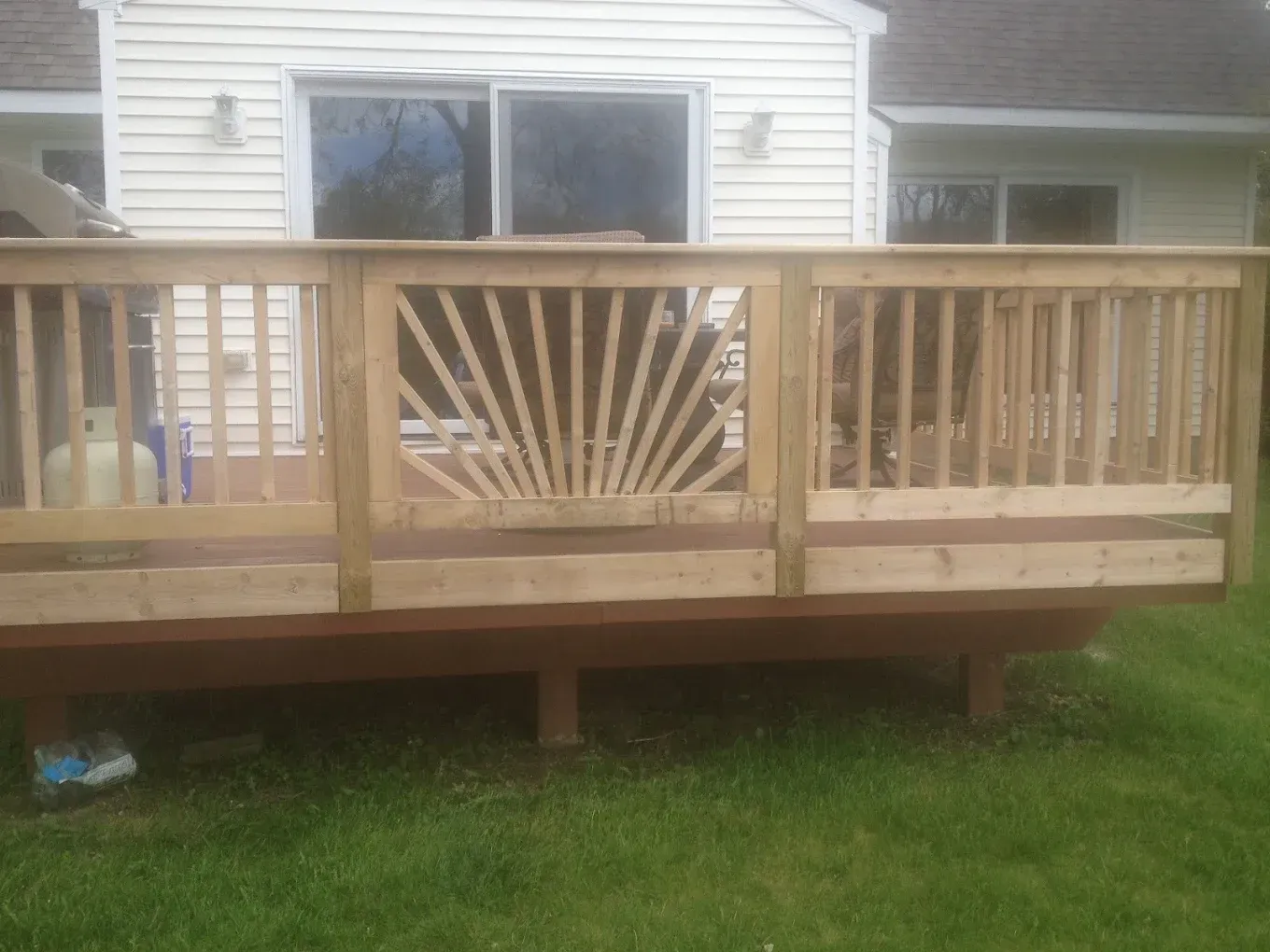 Wooden deck with decorative sunburst design, brown stain, and green lawn.