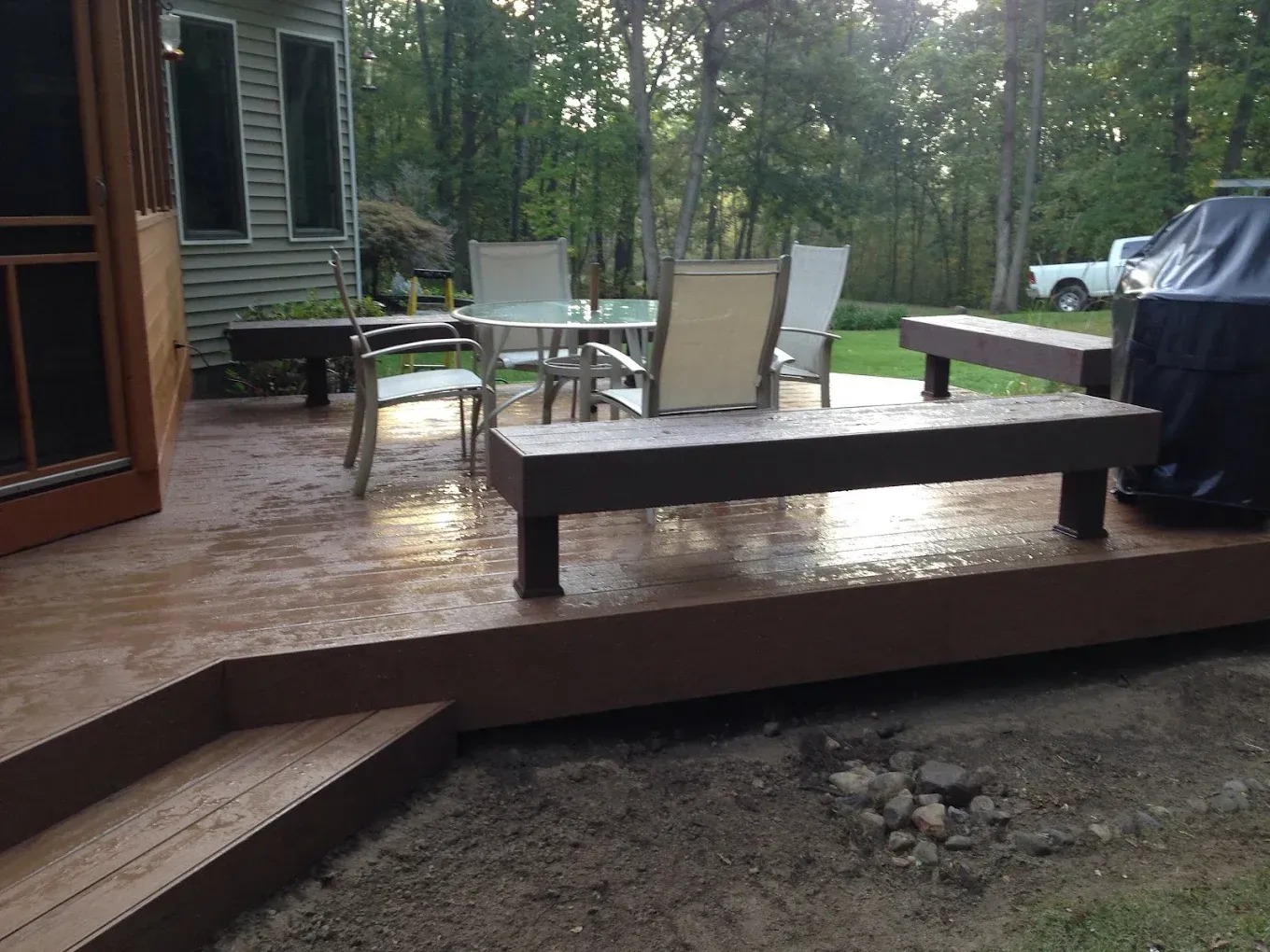 Outdoor deck with seating, table, grill, and surrounding trees.