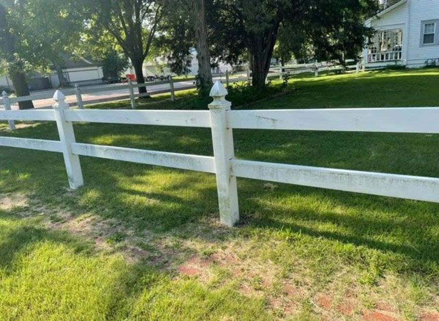 A white fence surrounds a lush green field in front of a house.