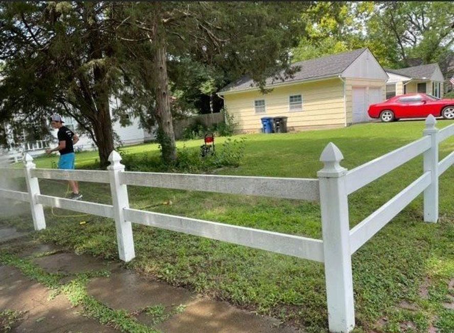 A white fence surrounds a house with a red car parked in front of it.