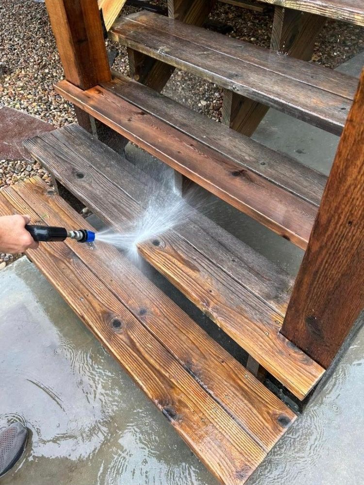 A person is using a high pressure washer to clean wooden stairs.