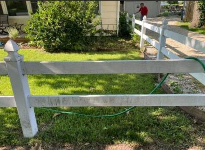 A white fence with a green hose attached to it in front of a house.